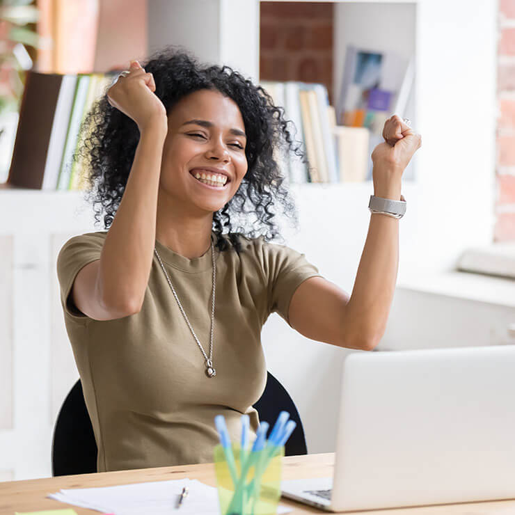 Small business woman cheering in front of her laptop after hiring a freelance copywriter.