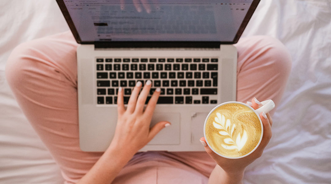 SEO copywriter Renee Mariette working on a laptop in bed with a coffee.